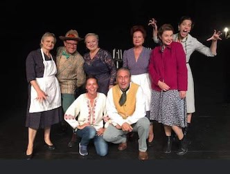 Une troupe de théâtre sur scène lors d'une représentation, avec un groupe de huit acteurs en costumes variés, sourire, et pose expressive, théâtre en action, piéce de théâtre avec ambiance conviviale.